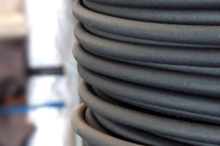 Close-up van een strak opgerolde zwarte kabel tegen een wazige achtergrond van werkplaatsgereedschap, wat wijst op een industriële omgeving. De uitstraling is ordelijk en functioneel.