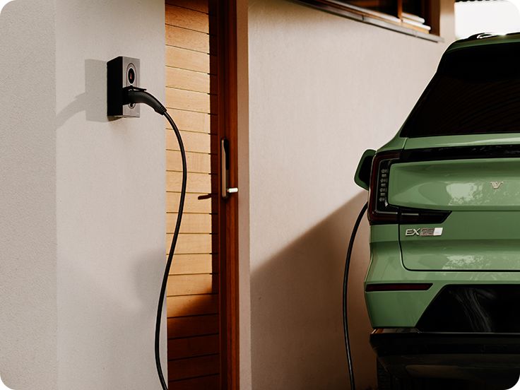 Eine Person hält ein Smartphone in der Nähe der an einer weißen Wand montierten Zaptec Go 2 Ladestation.