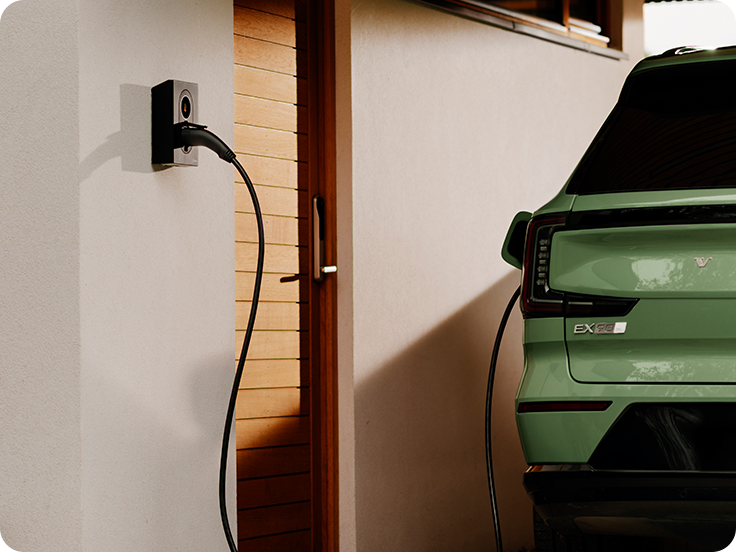 A person holds a smartphone near the Zaptec Go 2 charging station mounted on a white wall.