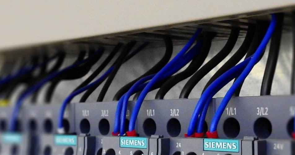 Close-up of a row of electrical terminal blocks with blue wires connected, in an industrial setting.
