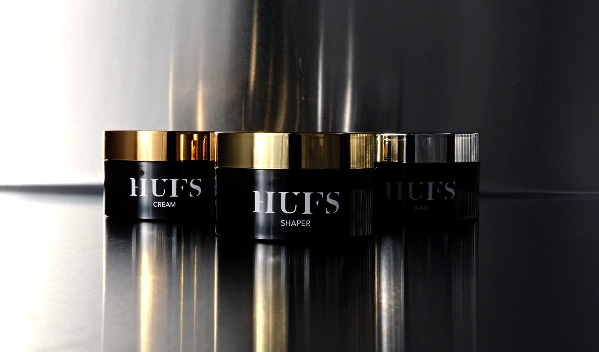 HUFS-tuotteita, kuten kerma, muotoilija ja vaha, mustissa purkeissa, joissa on kultaiset ja hopeiset kannet.