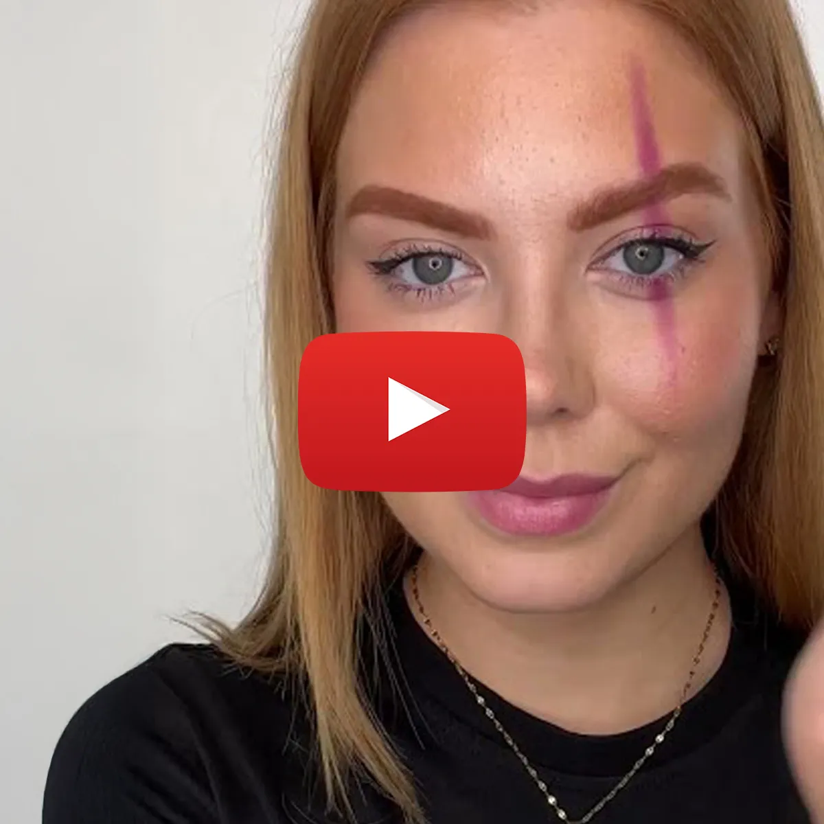 Närbild på en ung kvinna med långt rödblont hår och smink, med ett vertikalt streck av rosa färg över ena ögat. En YouTube-spelikon är överlagrad på bilden.