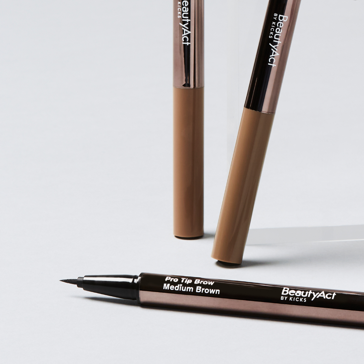 Tre ögonbrynspennor från BeautyAct, två ståendes, en liggandes mot en grå bakgrund