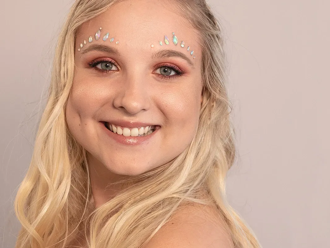 Smilende blond kvinne med kobberfarget øyenskygge og rhinestones på toppen av øyenbrynene.