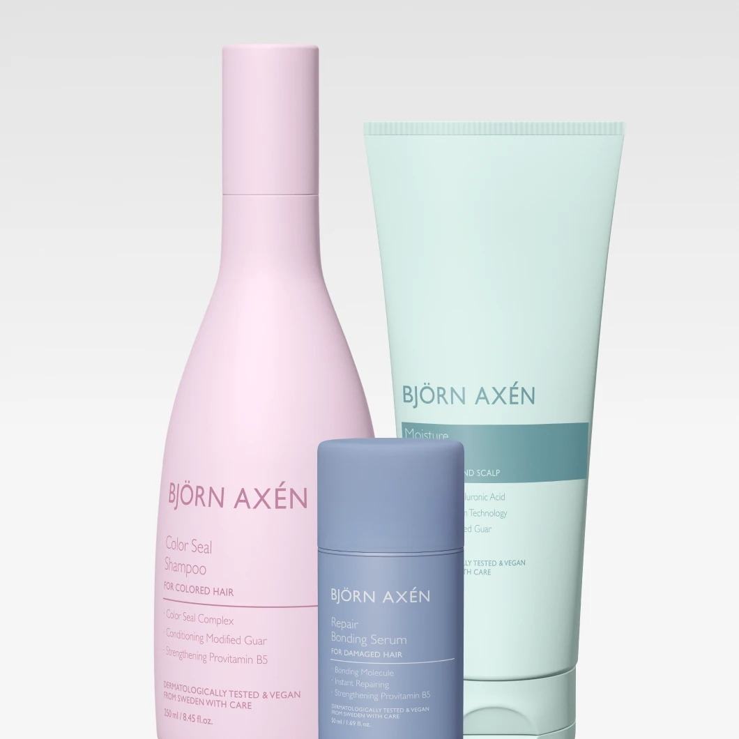 Björn Axén hårvårdsprodukter mot ljus bakgrund: Color Seal Shampoo i rosa flaska, Moisture Hair Mask i ljusgrön tub och Repair Bonding Serum i blå flaska, placerade bredvid varandra.