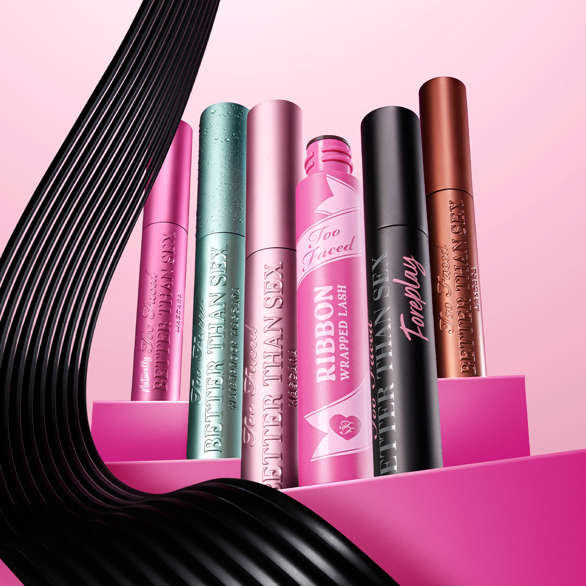 Kuusi eriväristä Too Faced -ripsiväriä vaaleanpunaisella taustalla. Vasemmalta oikealle: pinkki, vihreä, vaaleanpunainen, vaaleanpunainen nauhakuvioitu, musta ja pronssinvärinen.