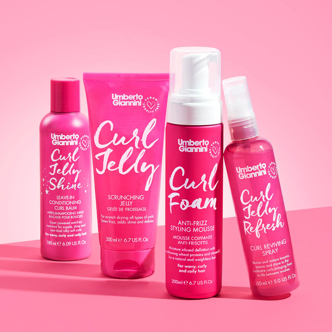 Fire Umberto Giannini-produkter, alle i knallrosa emballasje, står mot en lys rosa bakgrunn. Produktene er Curl Jelly Shine, Curl Jelly Scrunching Jelly, Curl Foam og Curl Jelly Refresh.