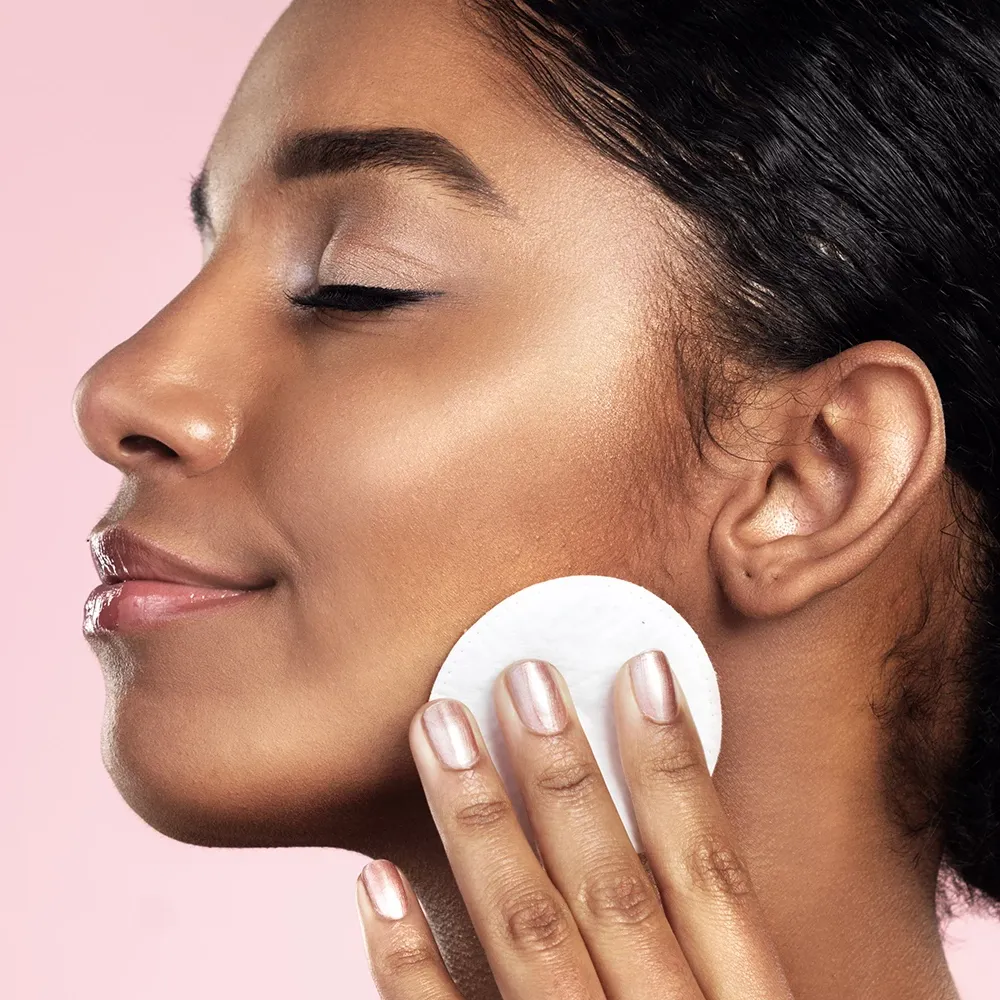 Hymyilevä henkilö, jolla on suljetut silmät, käyttää vanulappua kasvojen puhdistamiseen