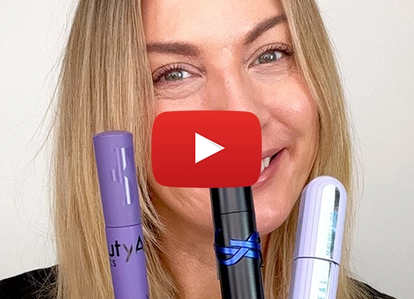 Makeup artist Petra med blondt hår visar upp tre mascara-produkter med ett brett leende 