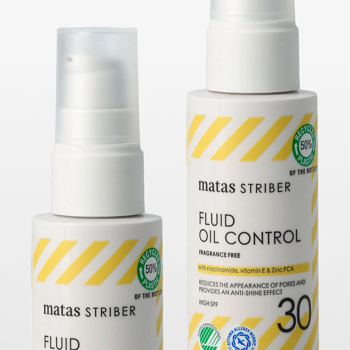 To hvite pumpeflasker fra Matas Striber Fluid Oil Control med gule diagonale striper og teksten “FRAGRANCE FREE”, “with niacinamide, vitamin E & Zinc PCA” samt “REDUCES THE APPEARANCE OF PORES AND PROVIDES AN ANTI-SHINE EFFECT”. Emballasjen viser også “HIGH SPF 30” og merkene “RECYCLED 50% PLASTIC”, “NORDIC SWAN ECOLABEL” og “ASTHMA ALLERGY NORDIC”.