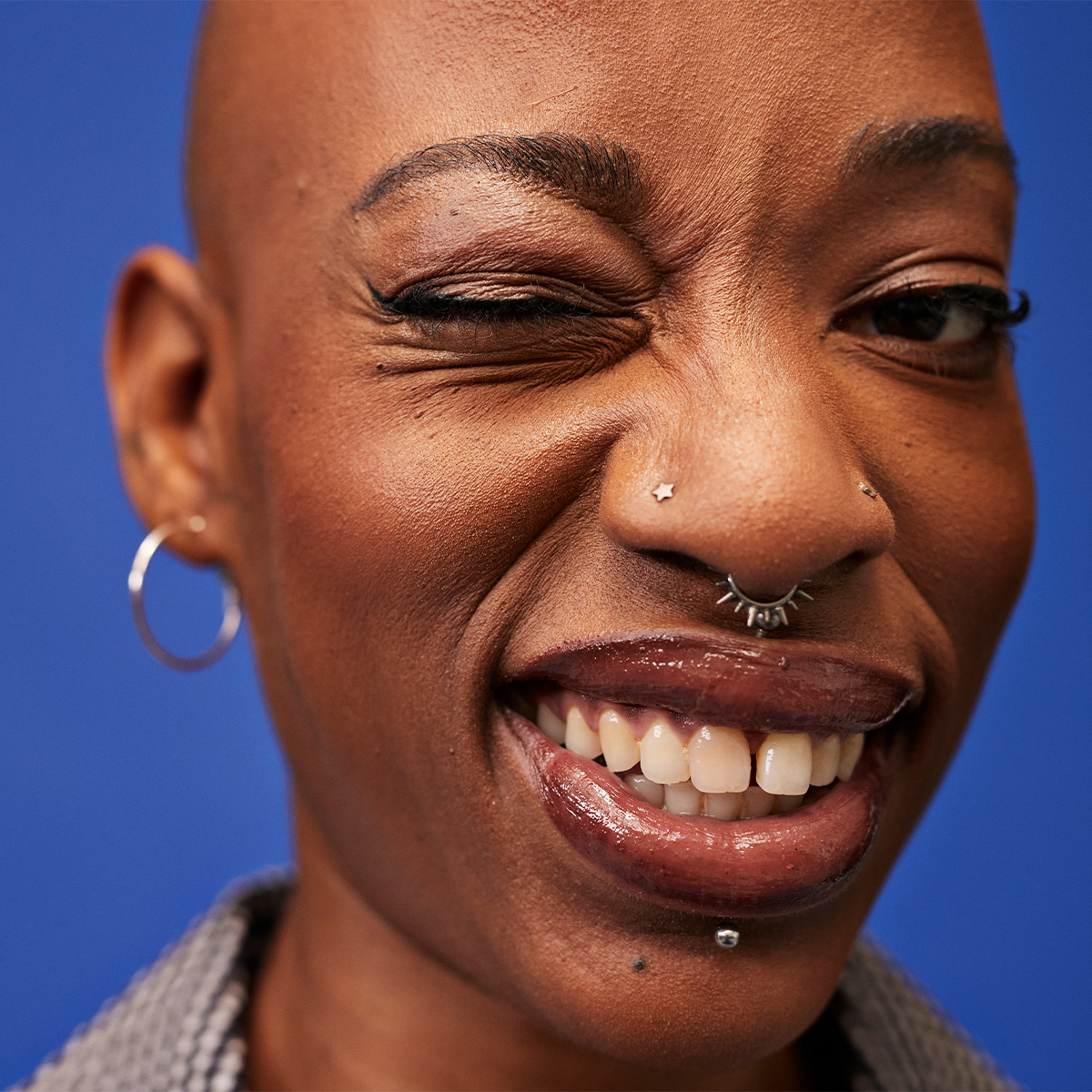 Person med blå bakgrund, silverörhänge och näspiercing.