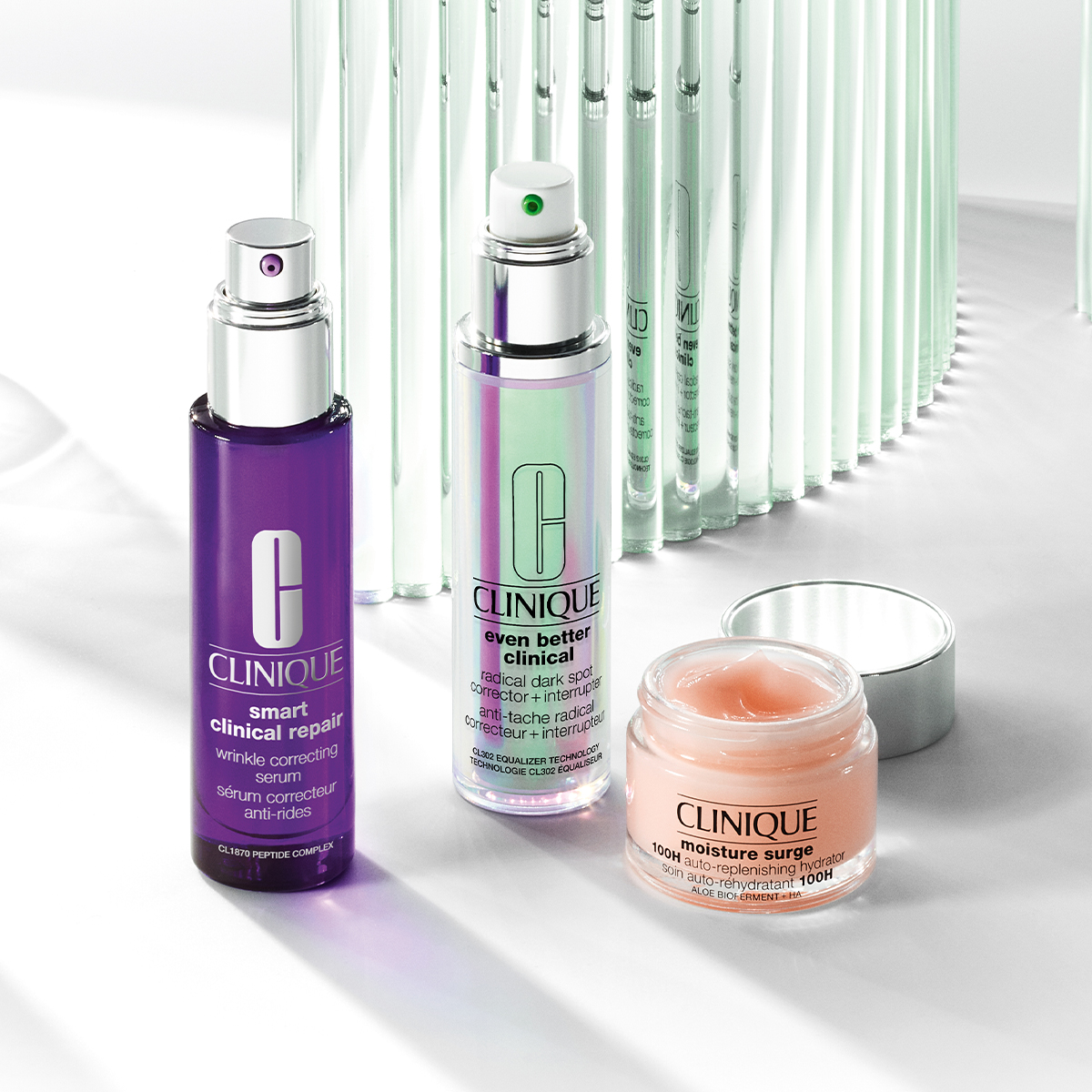 Tre hudvårdsprodukter från Clinique – två flaskor med pump och en öppen burk – placerade på en ljus yta med speglingar.
