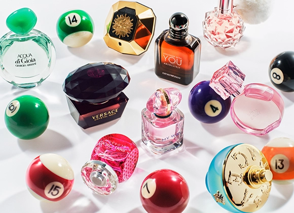 Bilde som viser flere parfymeflasker arrangert blant biljardkuler. Parfymene inkluderer Acqua di Gioia fra Giorgio Armani, Versace Crystal Noir, Stronger With You Intensely fra Emporio Armani, My Way fra Giorgio Armani, og andre. Bakgrunnen er hvit.