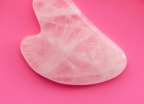 Rosa hjärtformad gua-sha sten mot cerise bakgrund.