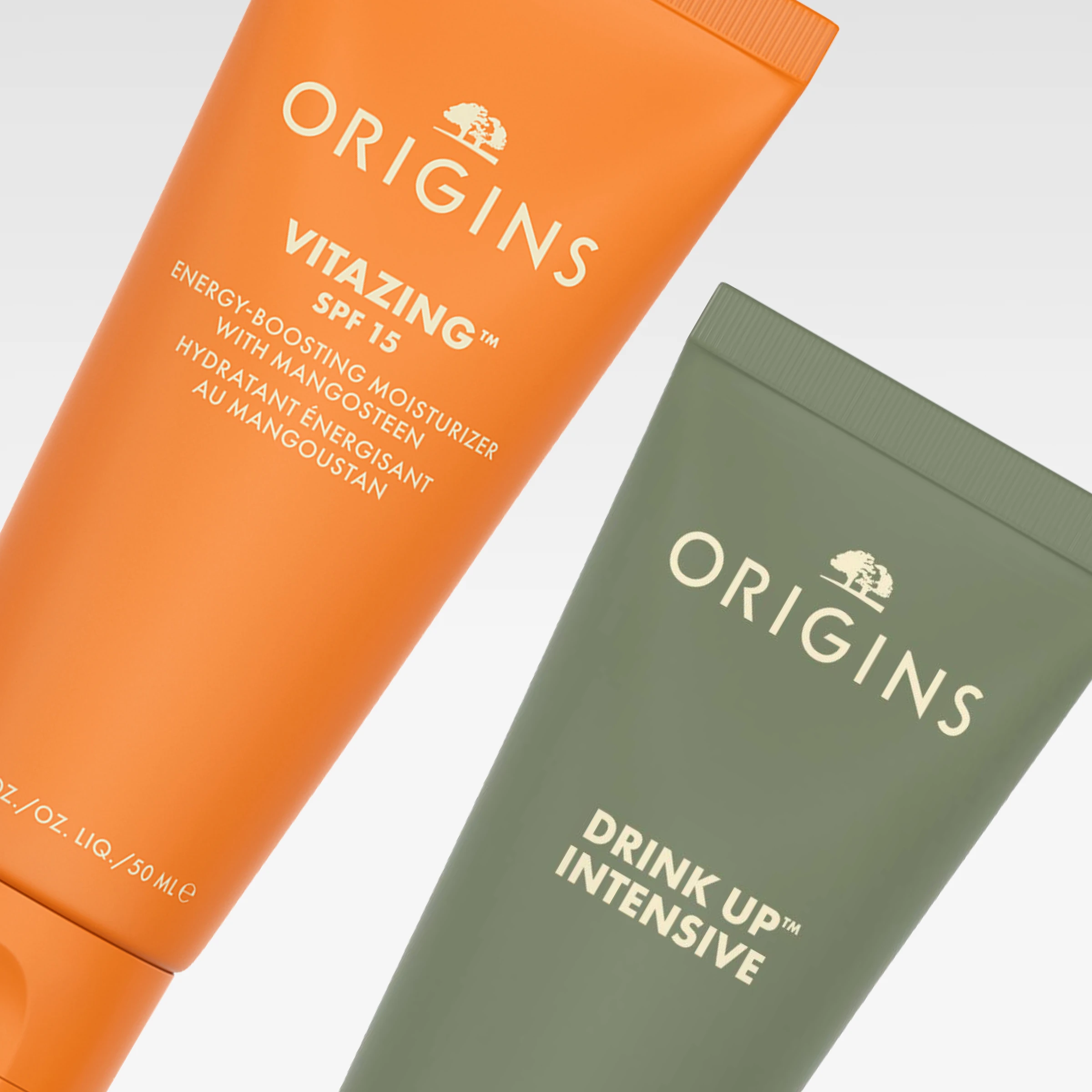 Origins-ihonhoitotuotteet oranssissa ja vihreässä tuubissa, mukana VitaZing SPF 15 ja Drink Up Intensive vaaleanharmaata taustaa vasten. Näkyvä teksti sisältää “energy-boosting moisturizer with mangosteen” ja “hydratant énergisant au mangoustan”.