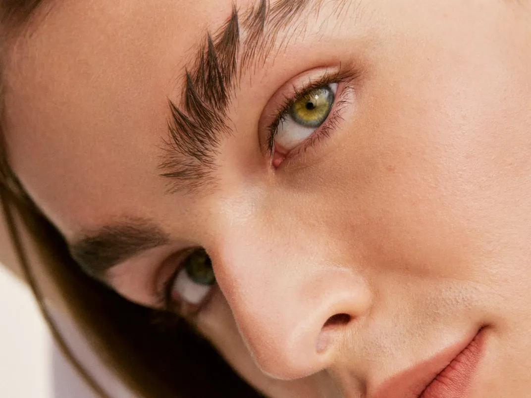 Människoansikte med gröna ögon, välvårdade ögonbryn och naturlig makeup.