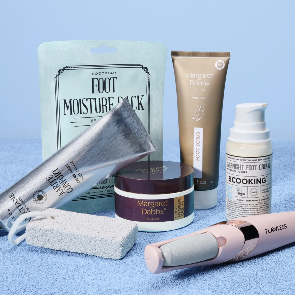Jalkojenhoitotuotteita vaaleansinistä taustaa vasten, mukana KOCOSTAR Foot Moisture Pack -jalkanaamio, Margaret Dabbs Foot Scrub ja Intensive Hydrating Foot Lotion sekä COOKING Underfoot Foot Cream. Kuvassa näkyy myös Flawless-sähköinen jalkaviila, hopeinen jalkavoidetuubi ja valkoinen hohkakivi kuorivaan ja pehmentävään jalkojenhoitoon kotona.