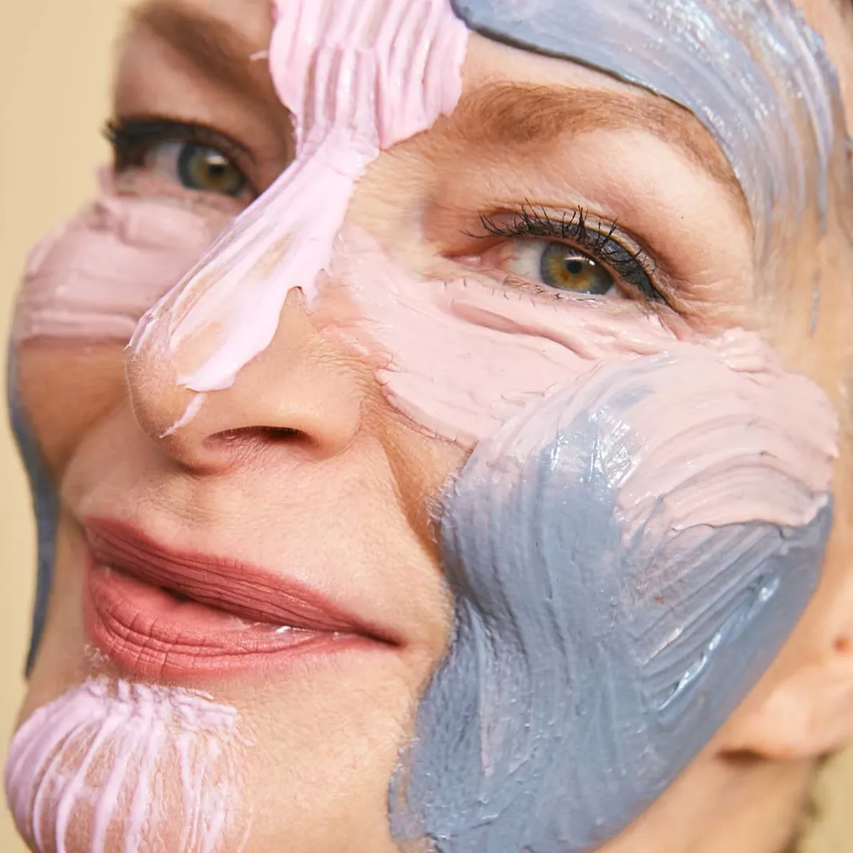 Närbild av kvinna med mogen hud som applicerat färgglada ansiktsmasker i olika zoner i ansiktet