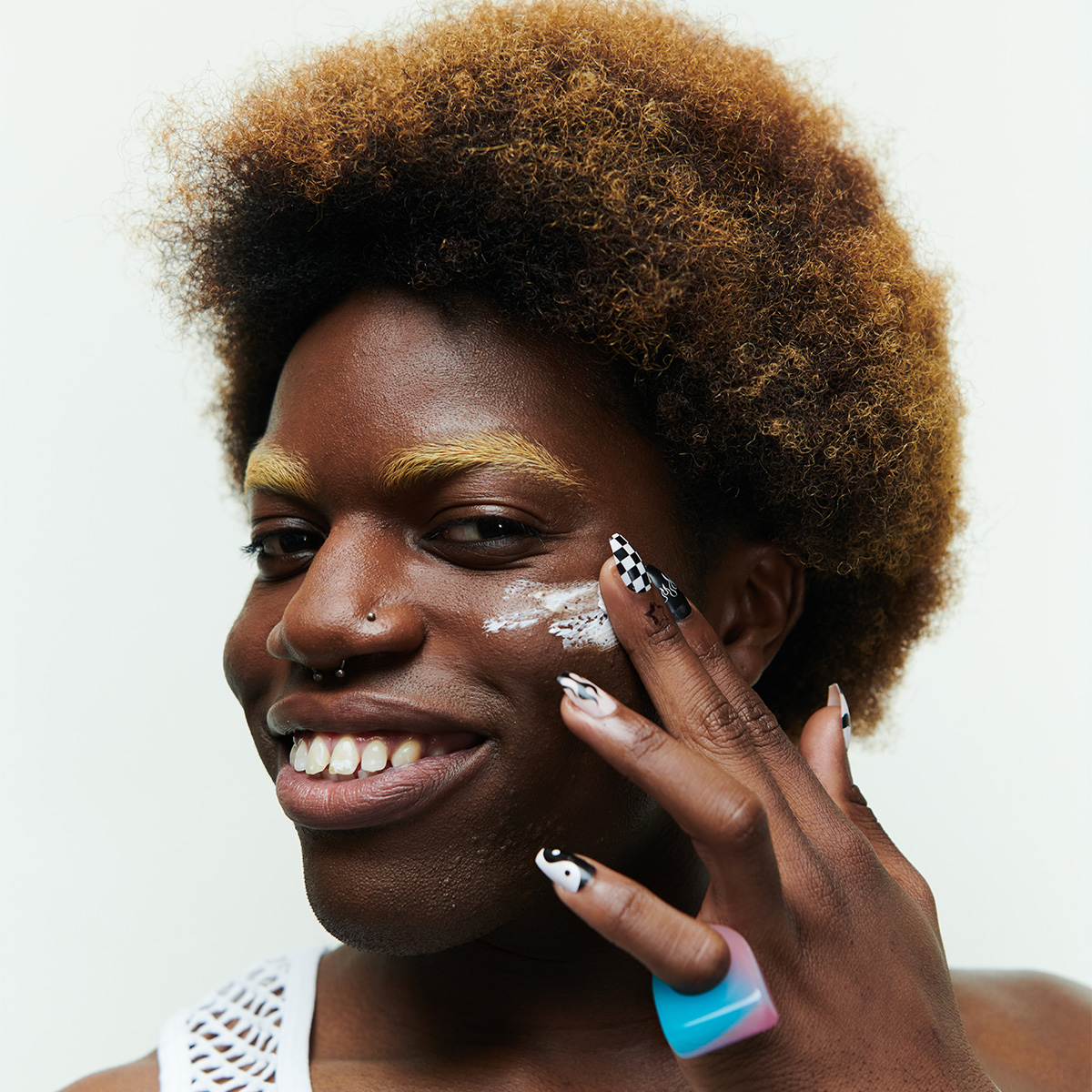 Hymyilevä kiharatukkainen henkilö levittää ihonhoitovoidetta kasvoilleen.