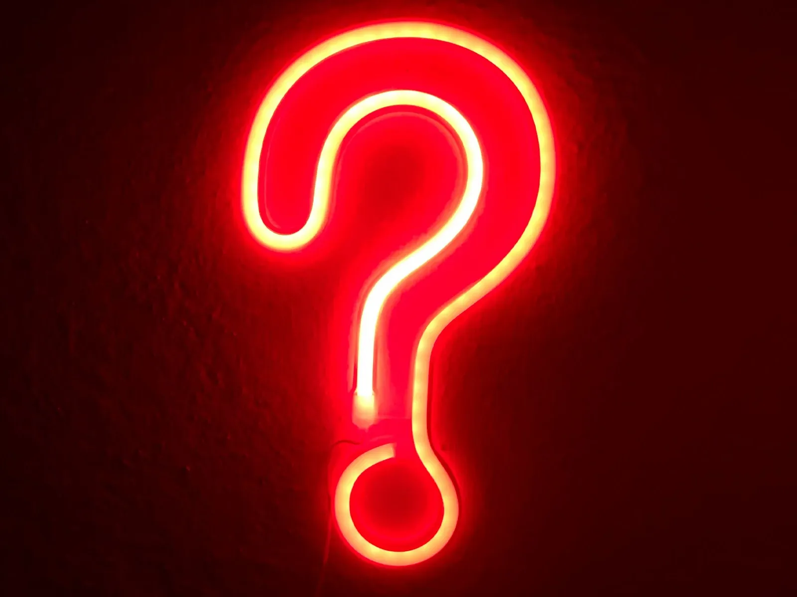 Lysande rött neonskylt i form av ett frågetecken mot mörk bakgrund.