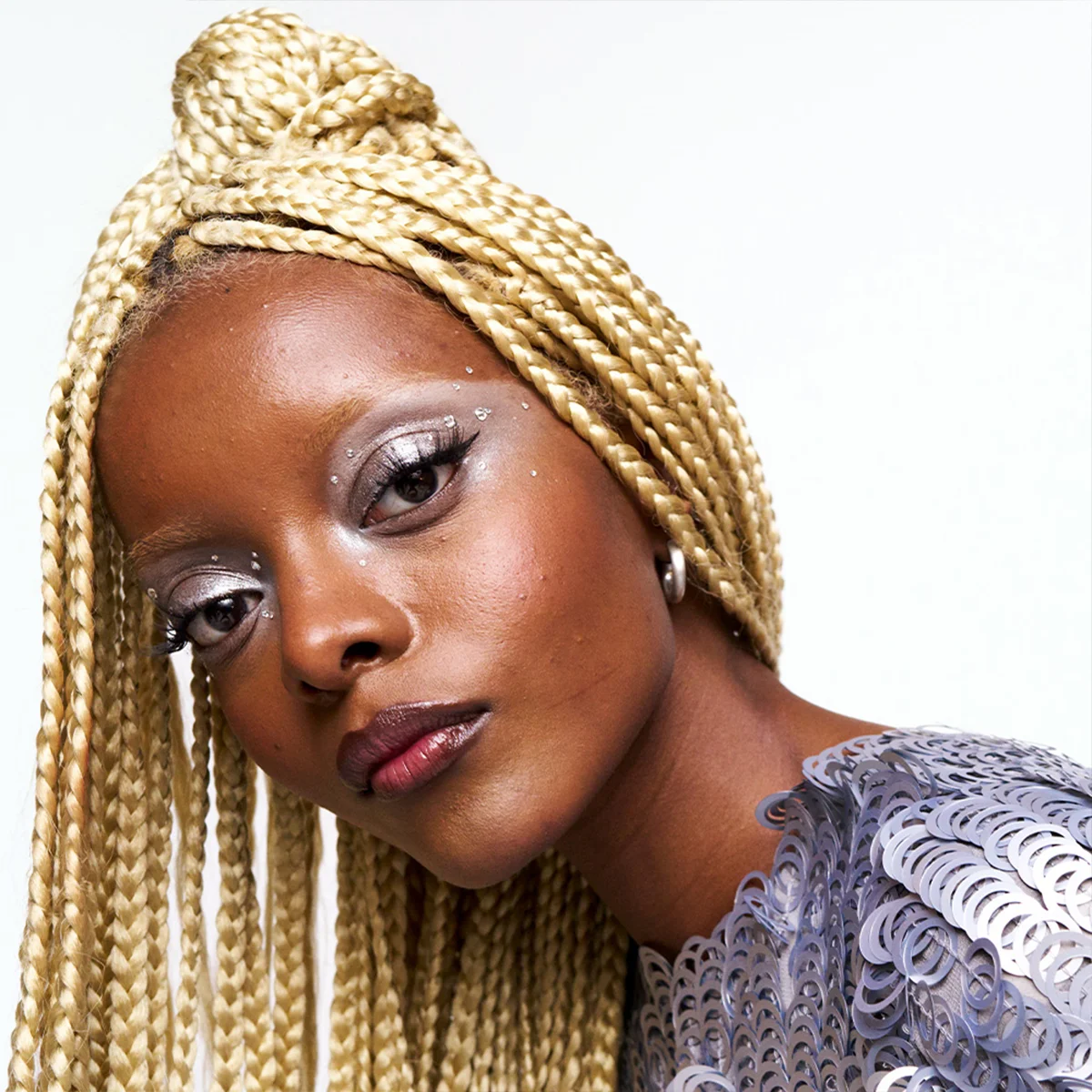 Modell med lange blonde fletter, metallisk øyenskygge og grafisk eyeliner – en inspirerende festlook med fokus på glød, trendy makeup og kreative beauty hacks