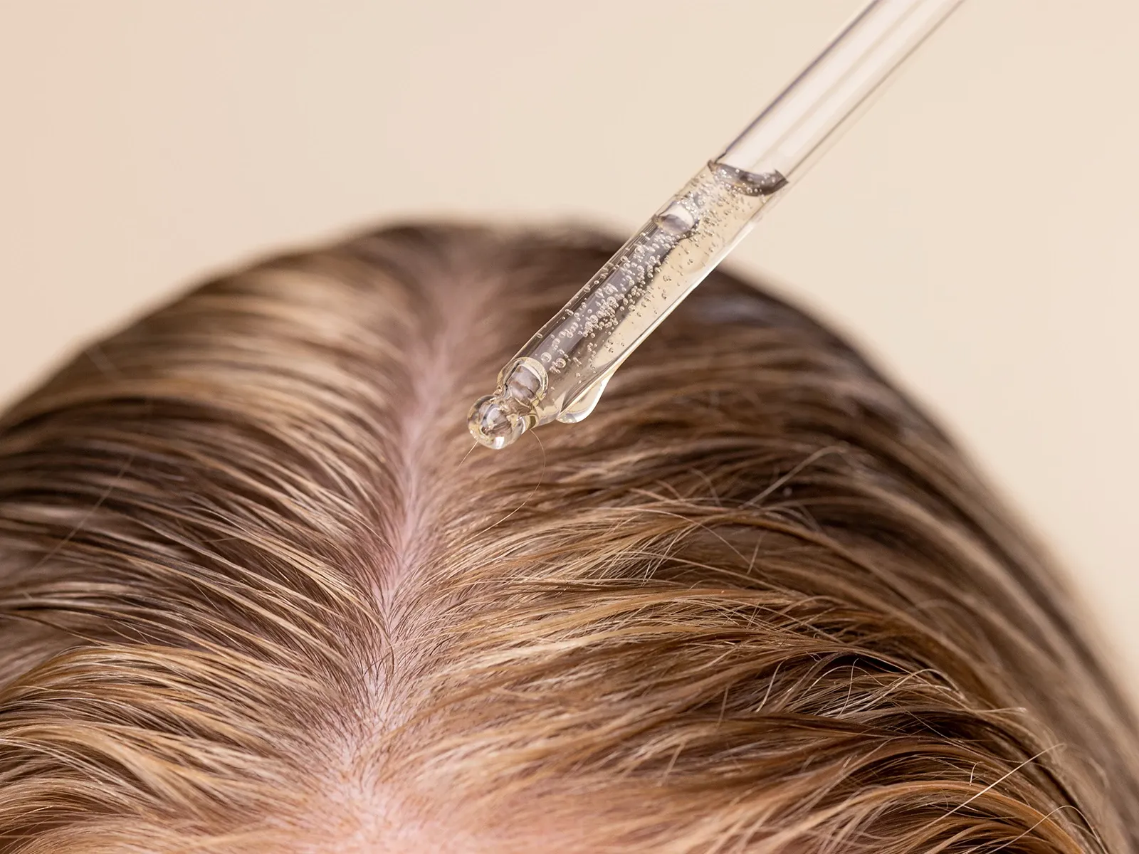 Hårbotten med ett serum som droppas på mot en beige bakgrund