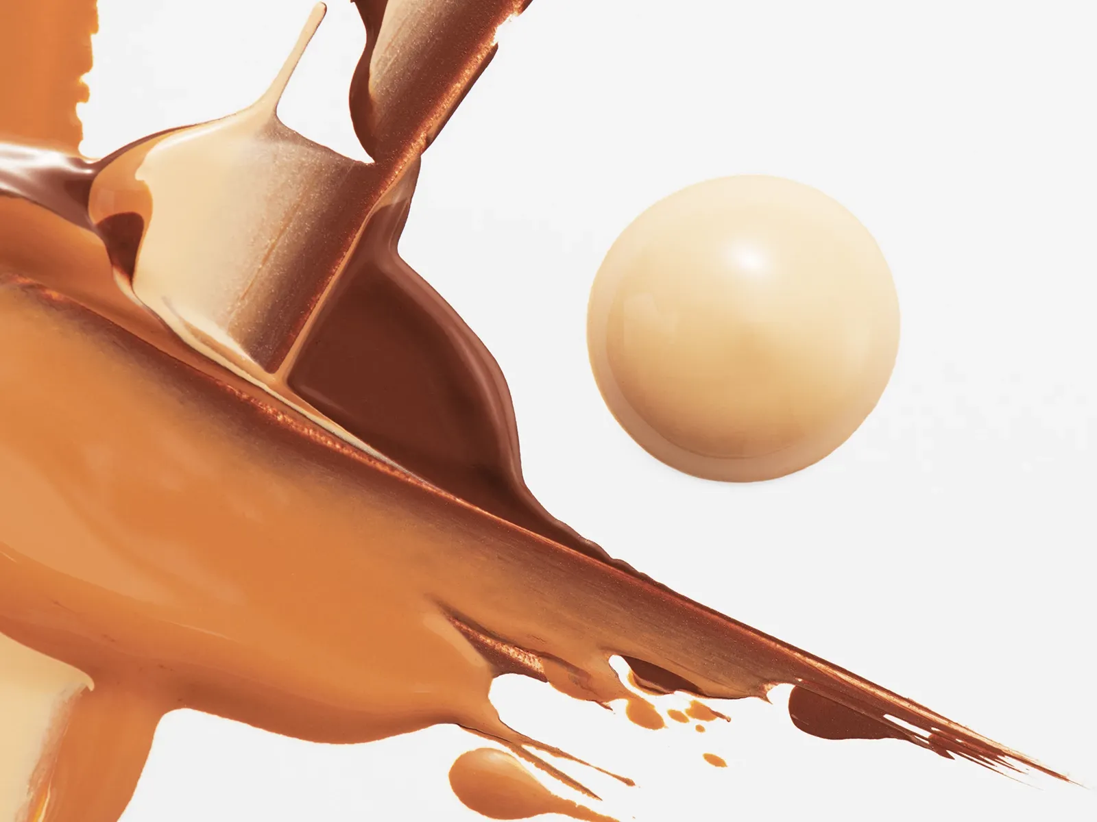 En concealer spredt i et abstrakt mønster i lysebrune toner, med en rund dråpe concealer ved siden – alt mot en hvit bakgrunn.