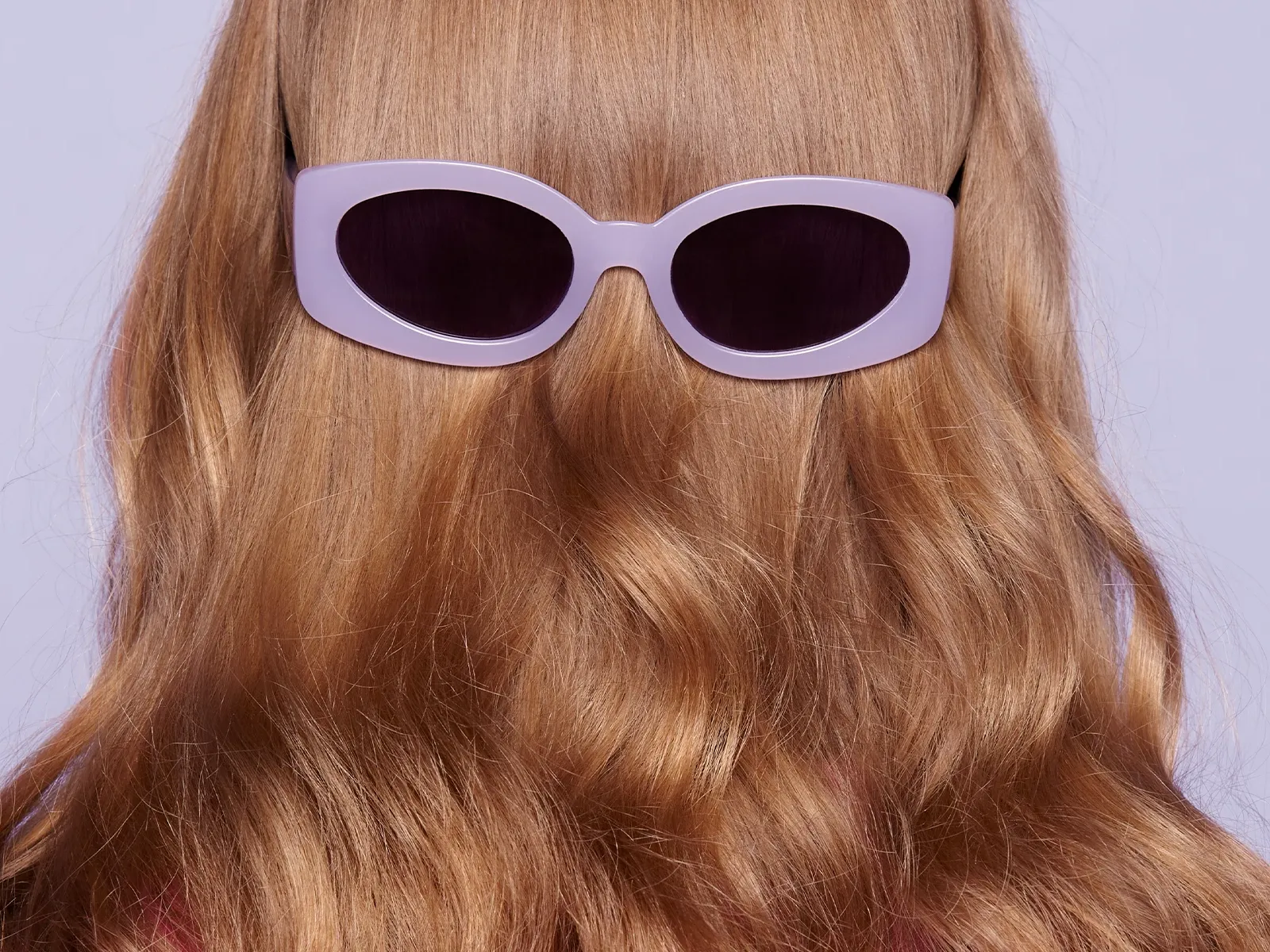 Baksiden av hodet på en person med langt oransje hår, med solbriller på bakvendt.