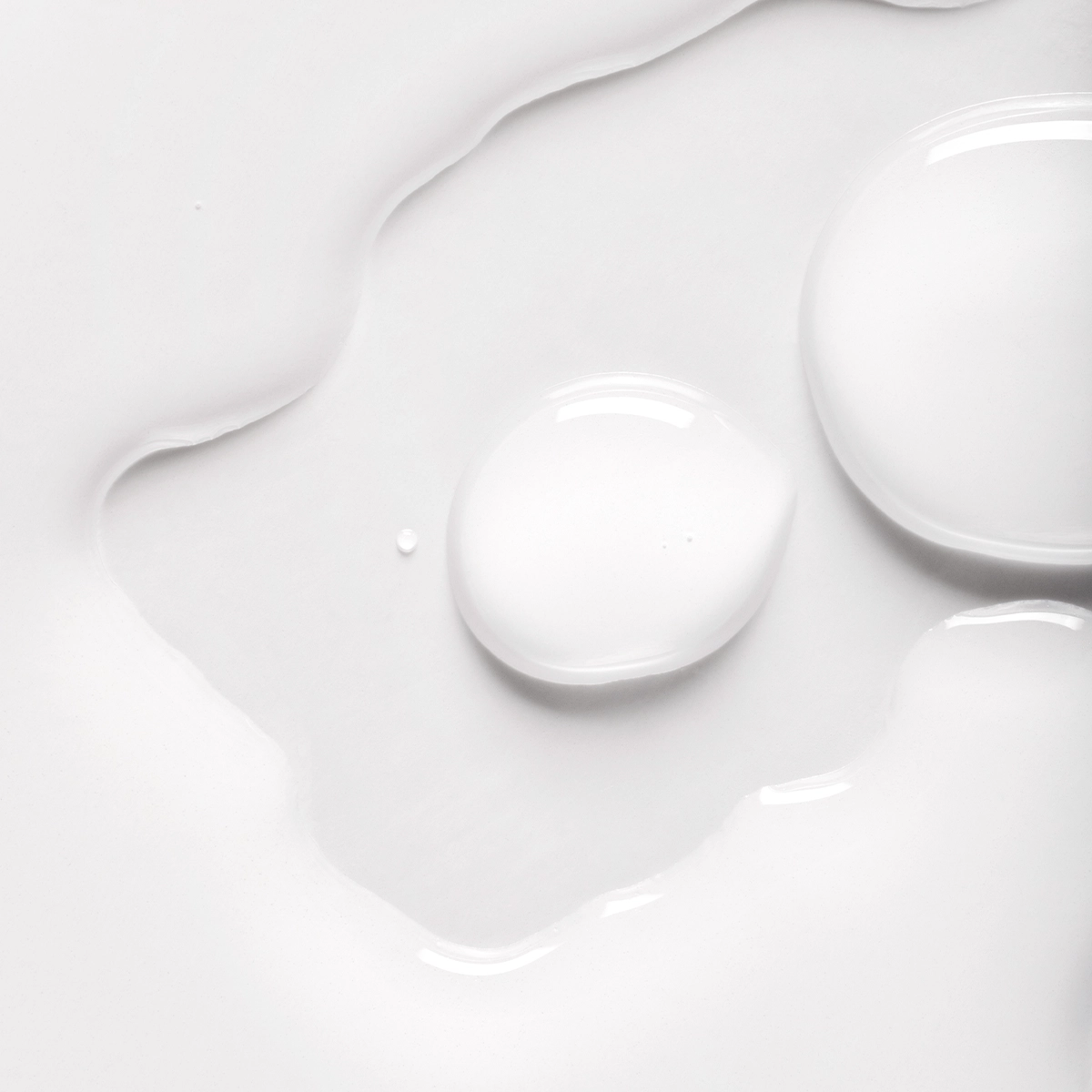 Nærbilde av transparent hudpleieserum i flytende form med myke dråper og glansfull overflate mot hvit bakgrunn. Minimalistisk teksturbilde som fremhever serumets konsistens innen skincare.