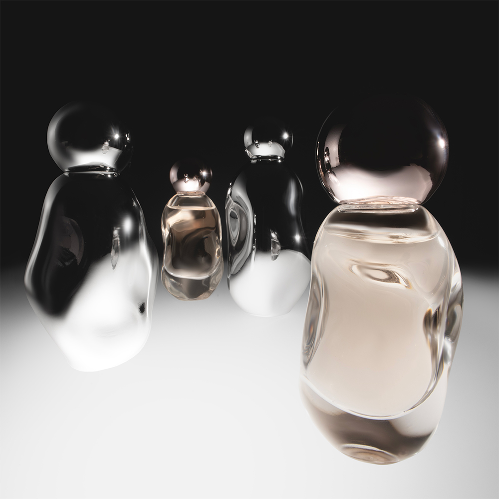 Neljä tyylikästä, pyöreämuotoista tuoksupulloa seisovat tummalla taustalla. Pullojen muotoilu on moderni ja minimalistinen, ja ne heijastavat valoa kauniisti.