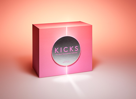 En rosa, lysande låda med Kicks-logga på framsidan, mot en bakgrund som tonas från vitt till orange.