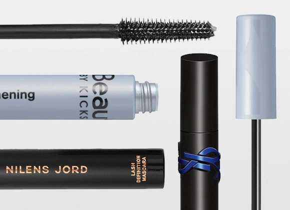 Flere mascaraer og børster fra KICKS Beauty og Nilens Jord med synlig tekst "Beauty by KICKS" og "NILENS JORD", sammen med svart mascarastruktur og åpne emballasjer på lys bakgrunn.