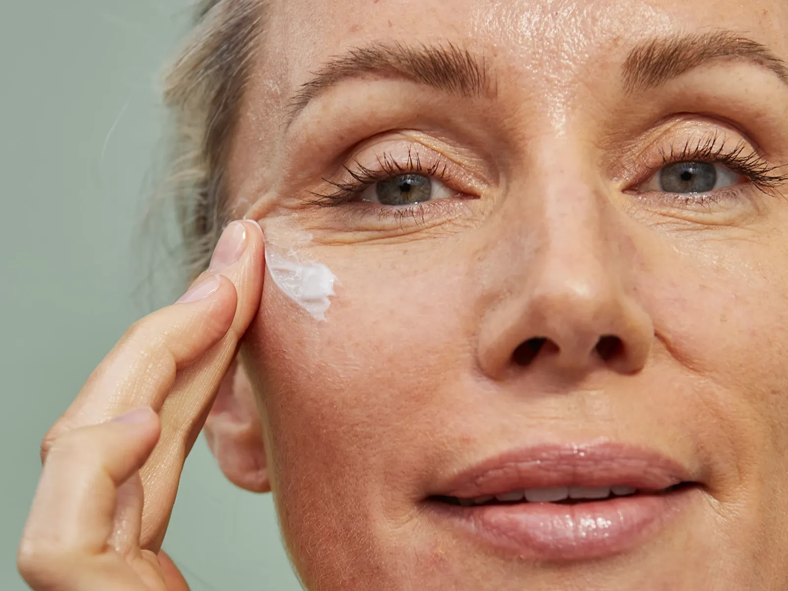 En person applicerar hudvårdsprodukt med fingrarna på sin kind.