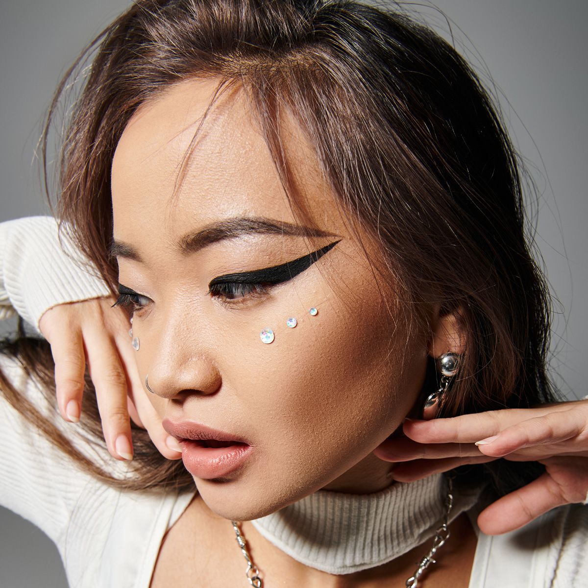 Kvinna med dramatisk eyeliner, ansiktsstenar i strass och snygga accessoarer.