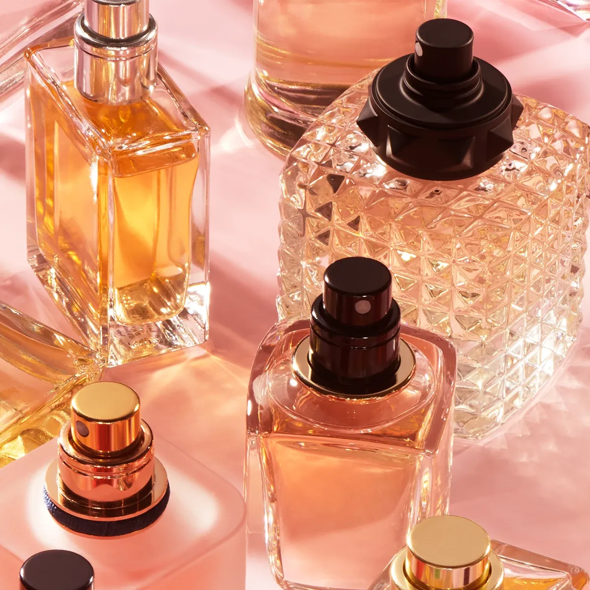 Vakre parfymeflasker i ulike former og farger på rosa bakgrunn