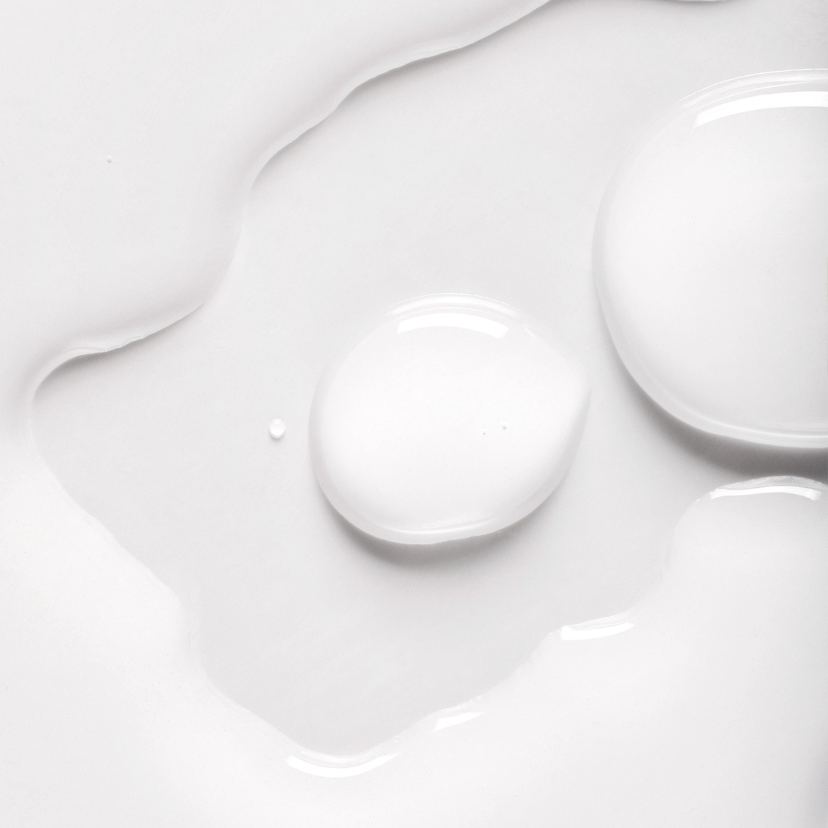 Närbild av vit hudvårdsprodukt med droppar och mjuk, glansig serum- eller lotiontextur mot vit bakgrund. Den krämiga konsistensen framhäver en återfuktande skincare-produkt med lätt och silkeslen finish.