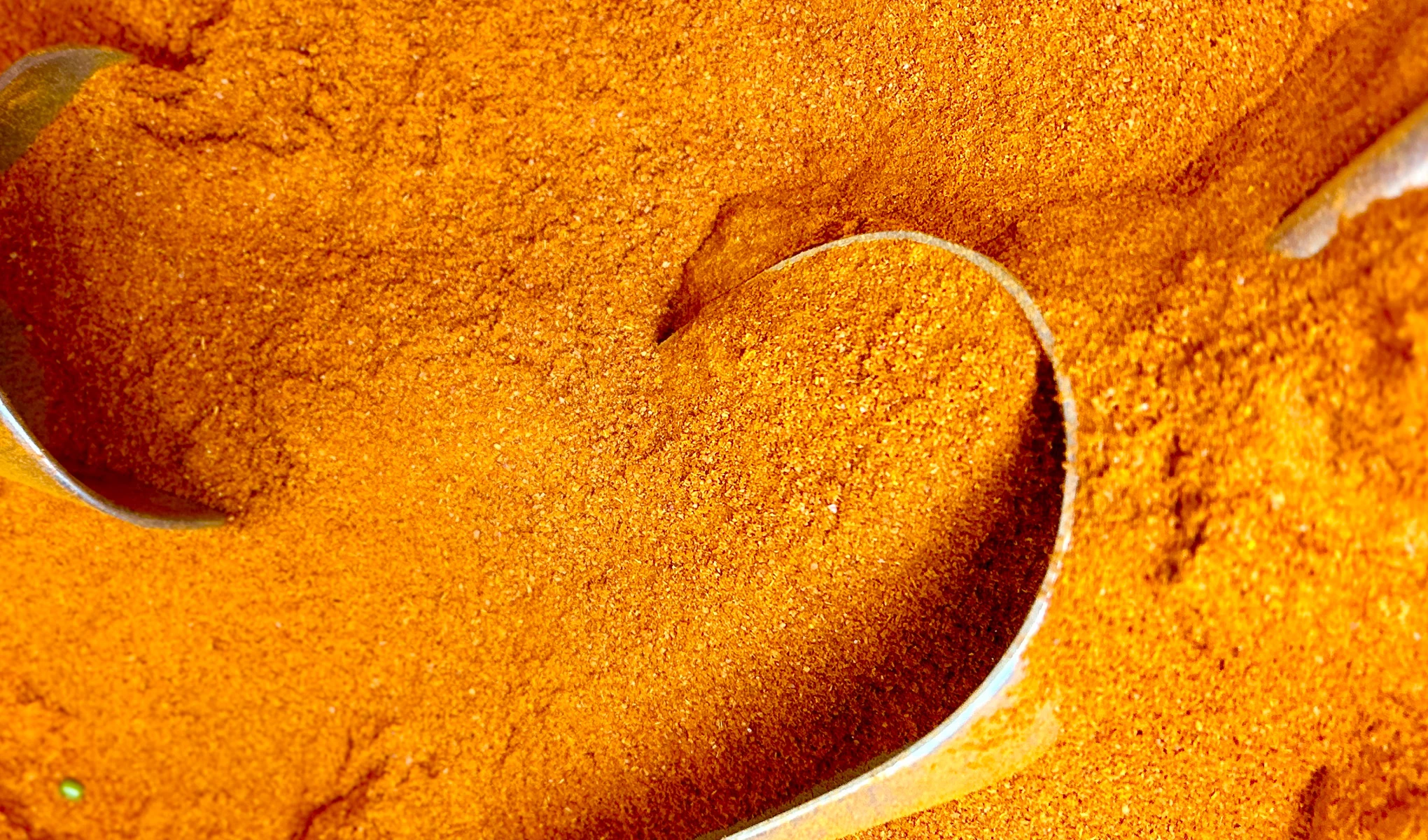 Oranssinsävyistä kurkumaa, jota nostetaan metallilusikoilla.