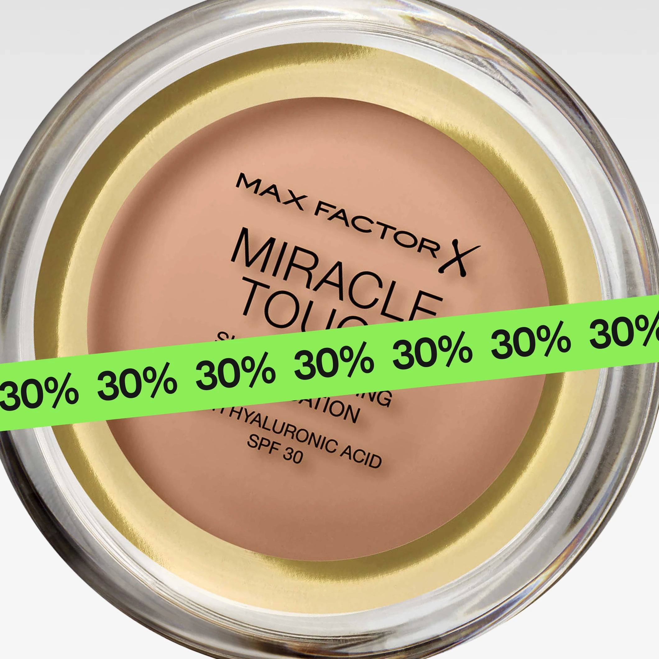 Lähikuva “Max Factor Miracle Touch Skin Perfecting Foundation with Hyaluronic Acid SPF 30” -meikkivoiteesta pyöreässä rasiassa, osittain vihreän “30%” -nauhan peitossa.