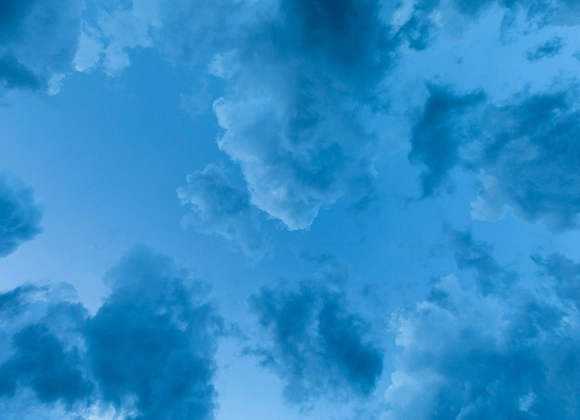 En klarblå himmel täckt av mörka, dramatiska moln som skapar en kontrast mot den ljusa bakgrunden.
