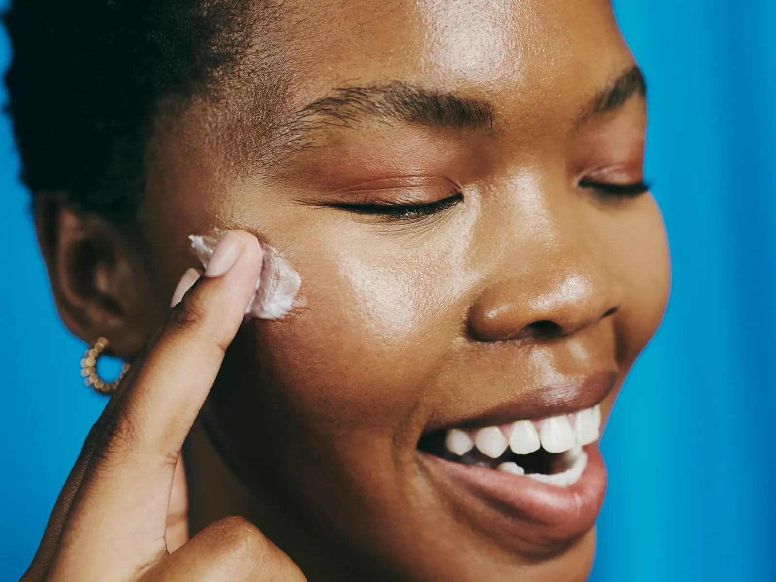 Lähikuva henkilöstä, jolla on sinistä luomiväriä ja kultainen korvarengas, sinistä taustaa vasten.