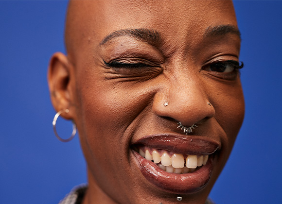 Person med blå bakgrunn, sølvøredobb og nesepiercing.