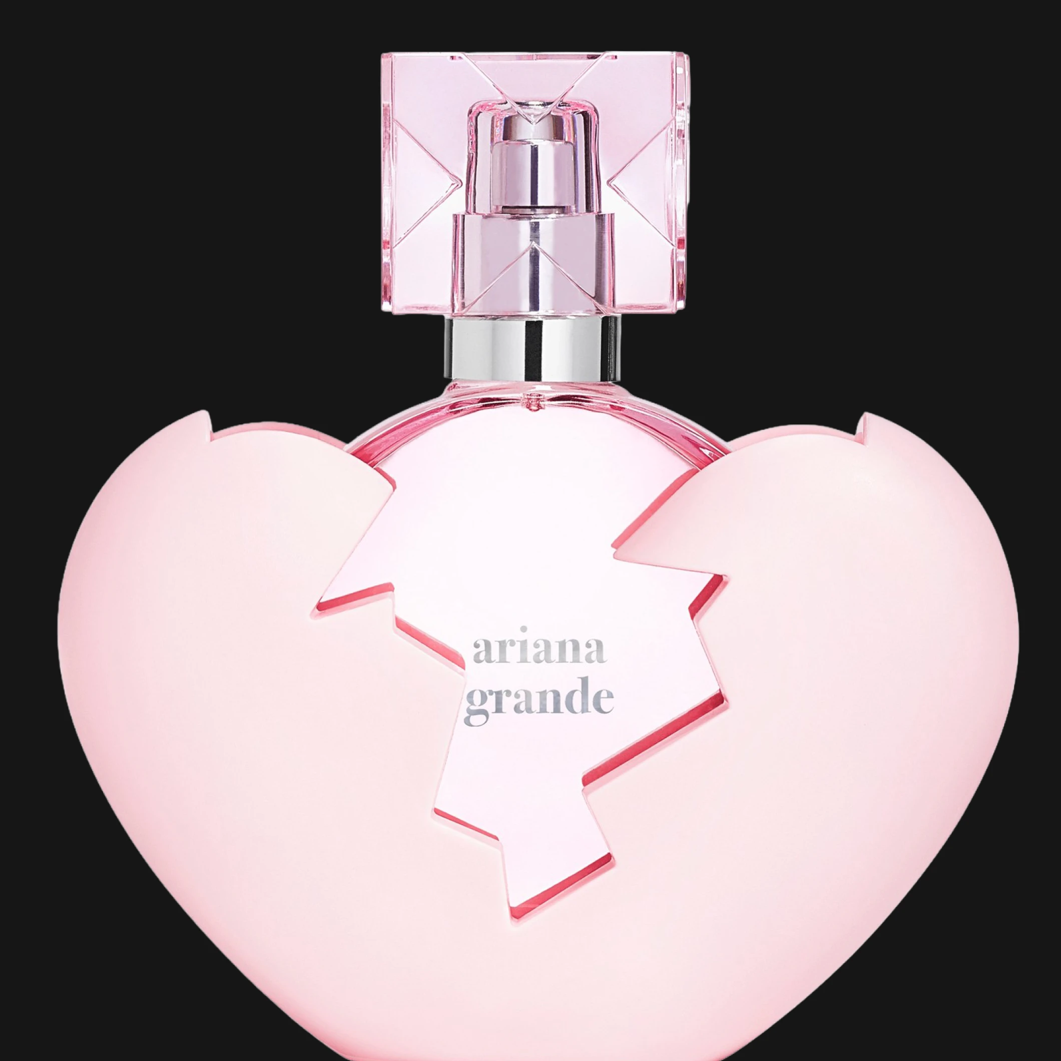 Ariana Grande parfymeflaske i rosa hjerteformet design med knust hjertemotiv og transparent rosa kork mot svart bakgrunn. Synlig tekst inkluderer “ariana grande”.