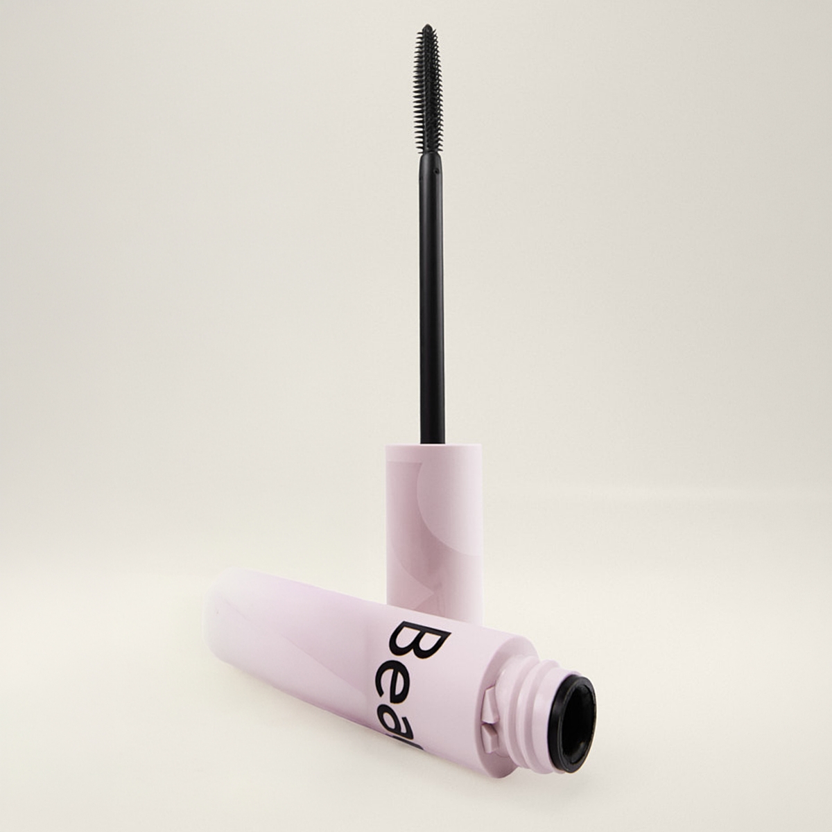 Öppen mascara från BeautyAct med ljusrosa hylsa och svart borste applicator mot ljus bakgrund, med synlig text “Bea” på förpackningen.