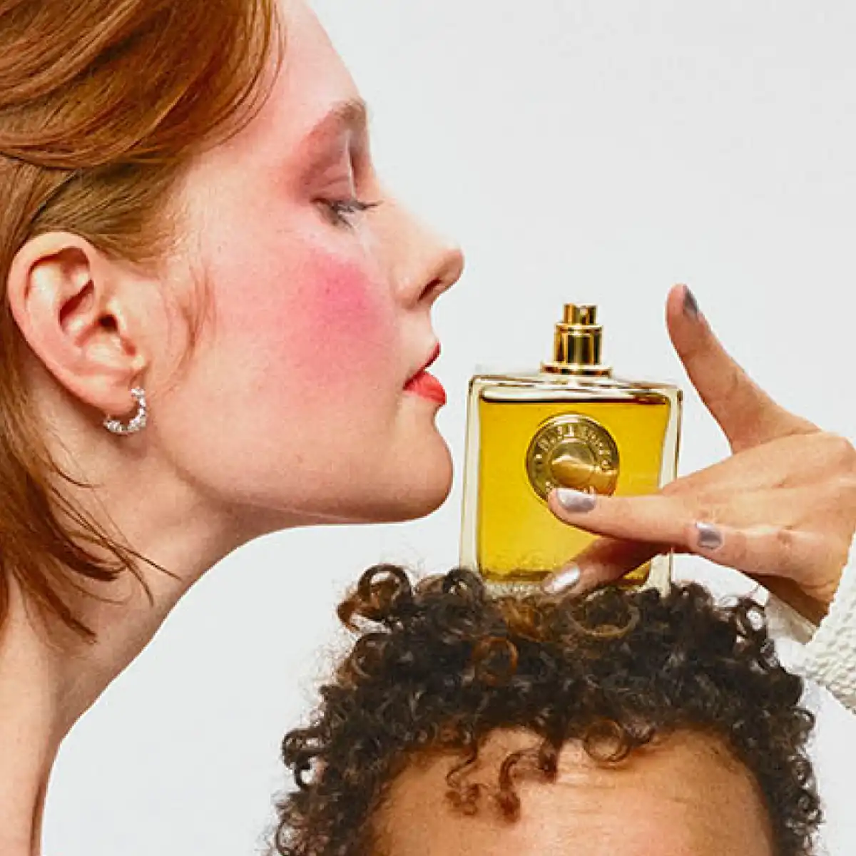 En person lutar sig fram för att dofta på en parfymflaska som hålls ovanpå en annan persons huvud.