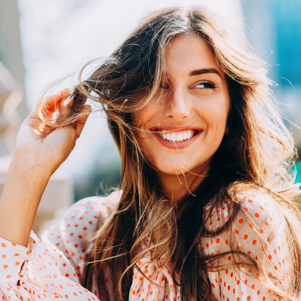 Hymyilevä tyttö, jolla on ruskeat hiukset pitelee hiussuortuvaa.