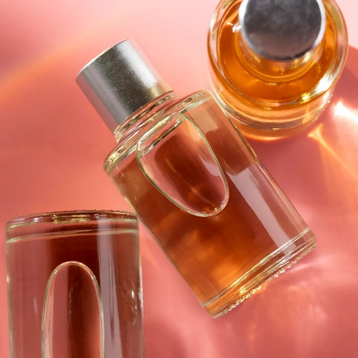 Tre parfymeflasker med oransje væske på en rosa bakgrunn.