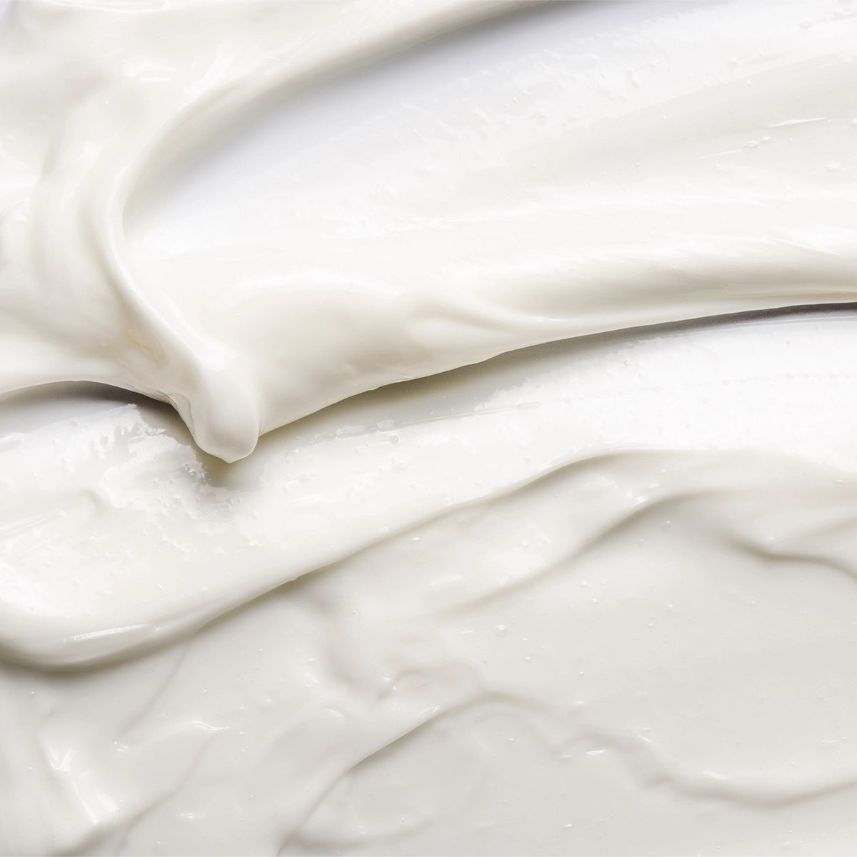 Närbild av en vit hudvårdskräm med mjuk, krämig konsistens utsmetad i böljande rörelser. Texturbild som framhäver en återfuktande ansiktskräm eller body lotion med glansig finish.