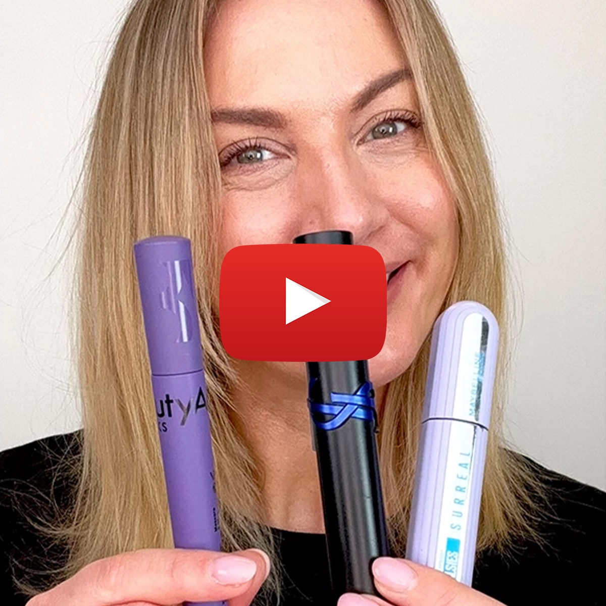 Makeup artist Petra med blondt hår visar upp tre mascara-produkter med ett brett leende