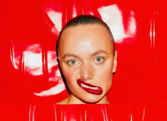 Nainen punaisella huulipunalla irvistää kirkkaanpunaisen taustan edessä.