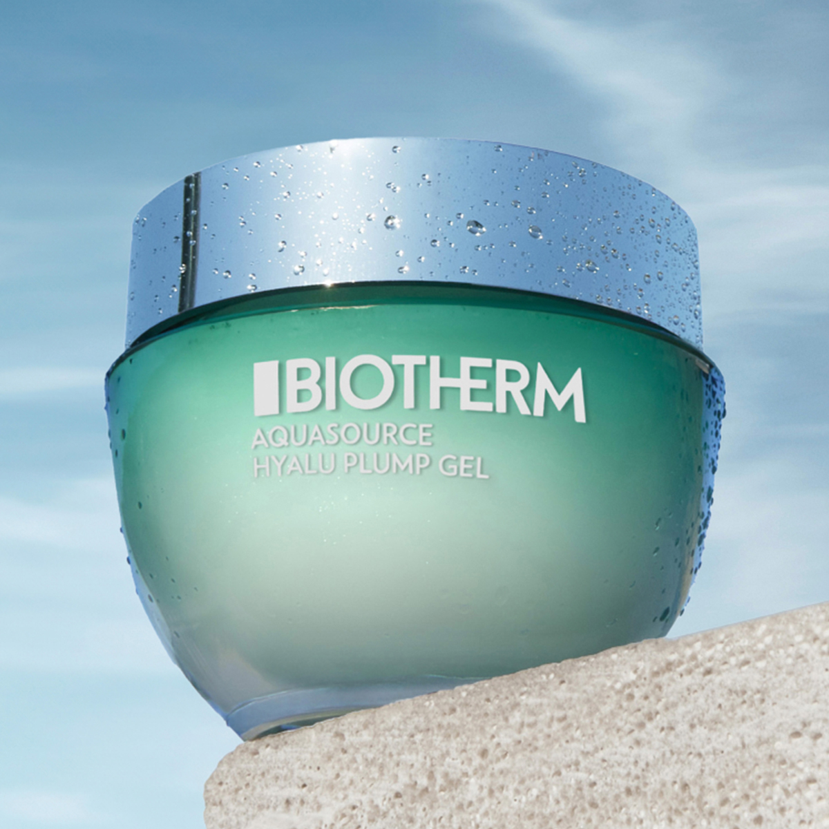 Aquasource Hyalu Plump Gel från Biotherm. Gelén kommer i en grön glasburk med ett silverlock och har texten "Biotherm Aquasource Hyalu Plump Gel" på framsidan. Burken står på en beige plattform mot en blå himmel med några vita moln.
